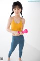 A woman in a yellow top and blue leggings holding a pink dumbbell.