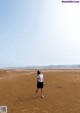 A woman standing on a sandy beach looking up at the sky.