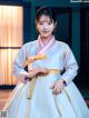 A woman in a white and pink hanbok is posing for a picture.