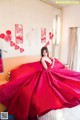 A woman in a red dress sitting on a bed.