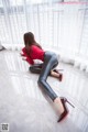 A woman in a red shirt and black leather pants crouching on the floor.