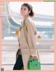 A woman in a beige coat holding a green handbag.