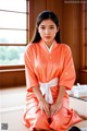 A woman in an orange kimono sitting on the floor.