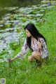 A woman kneeling in the grass next to a pond of water lilies.